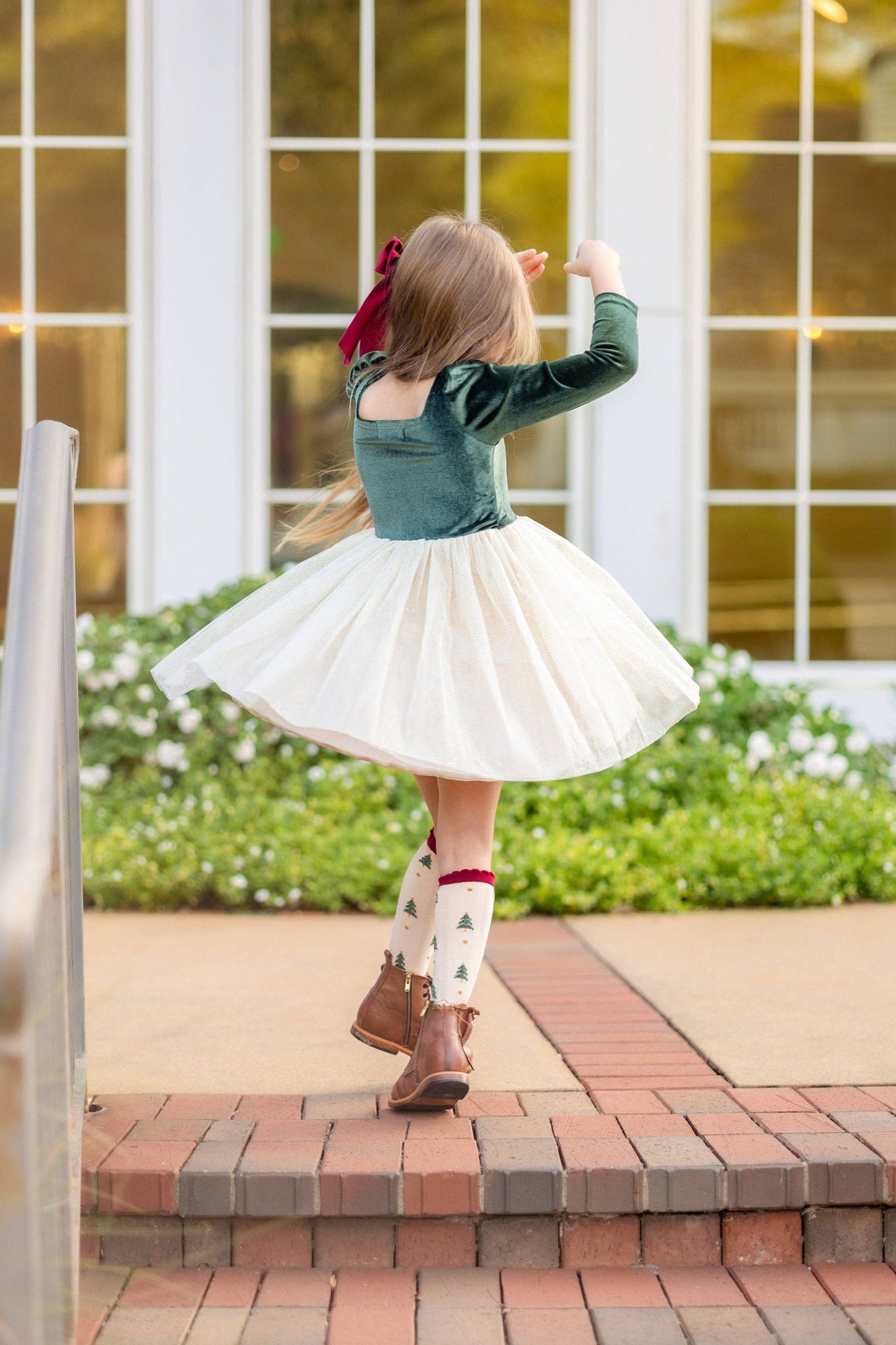 Child in a green top and white skirt dancing on a brick path with a building in the background