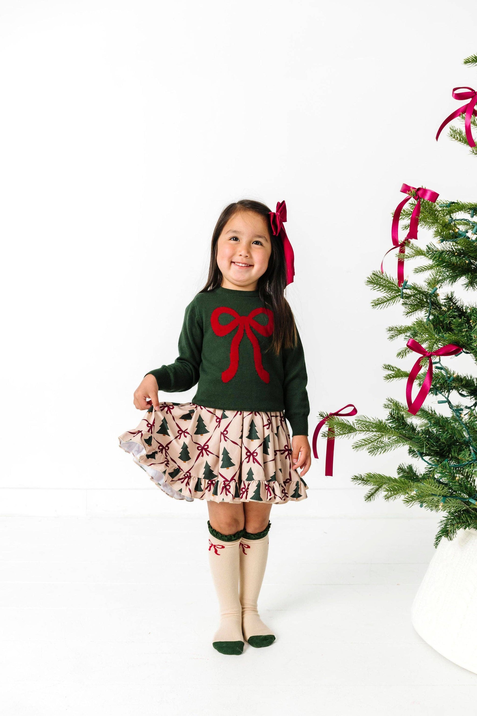 Young girl in festive outfit with Christmas tree and ribbons in the background