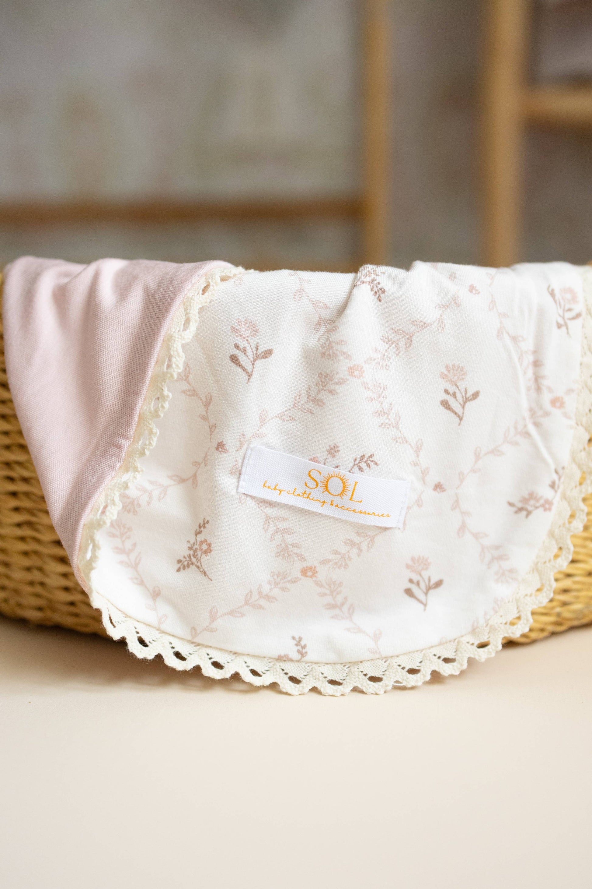 Baby blanket with lace edge and SOI logo on a wicker basket