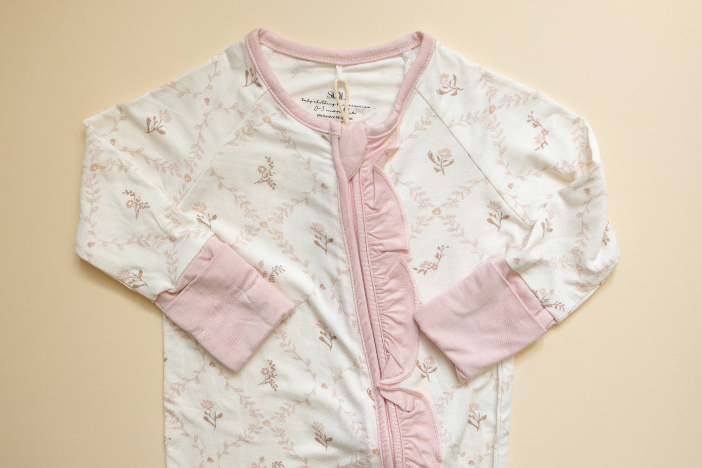 Baby outfit with floral pattern and pink accents on a beige background