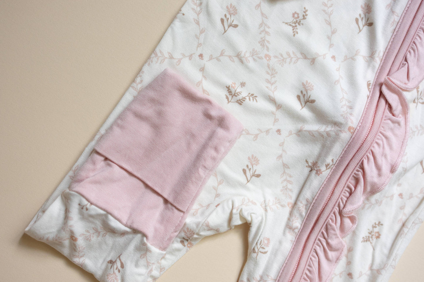 Pink baby blanket and hat on a floral quilt with a beige background