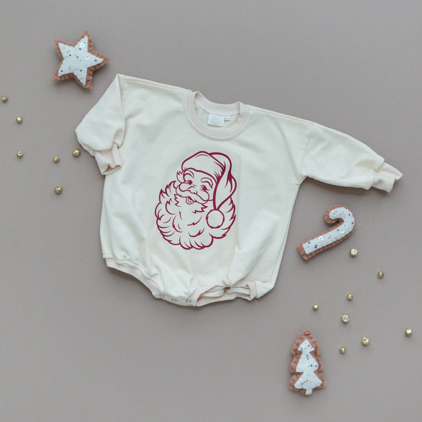 White baby onesie with red Santa hat design on a gray background with Christmas-themed cookies.
