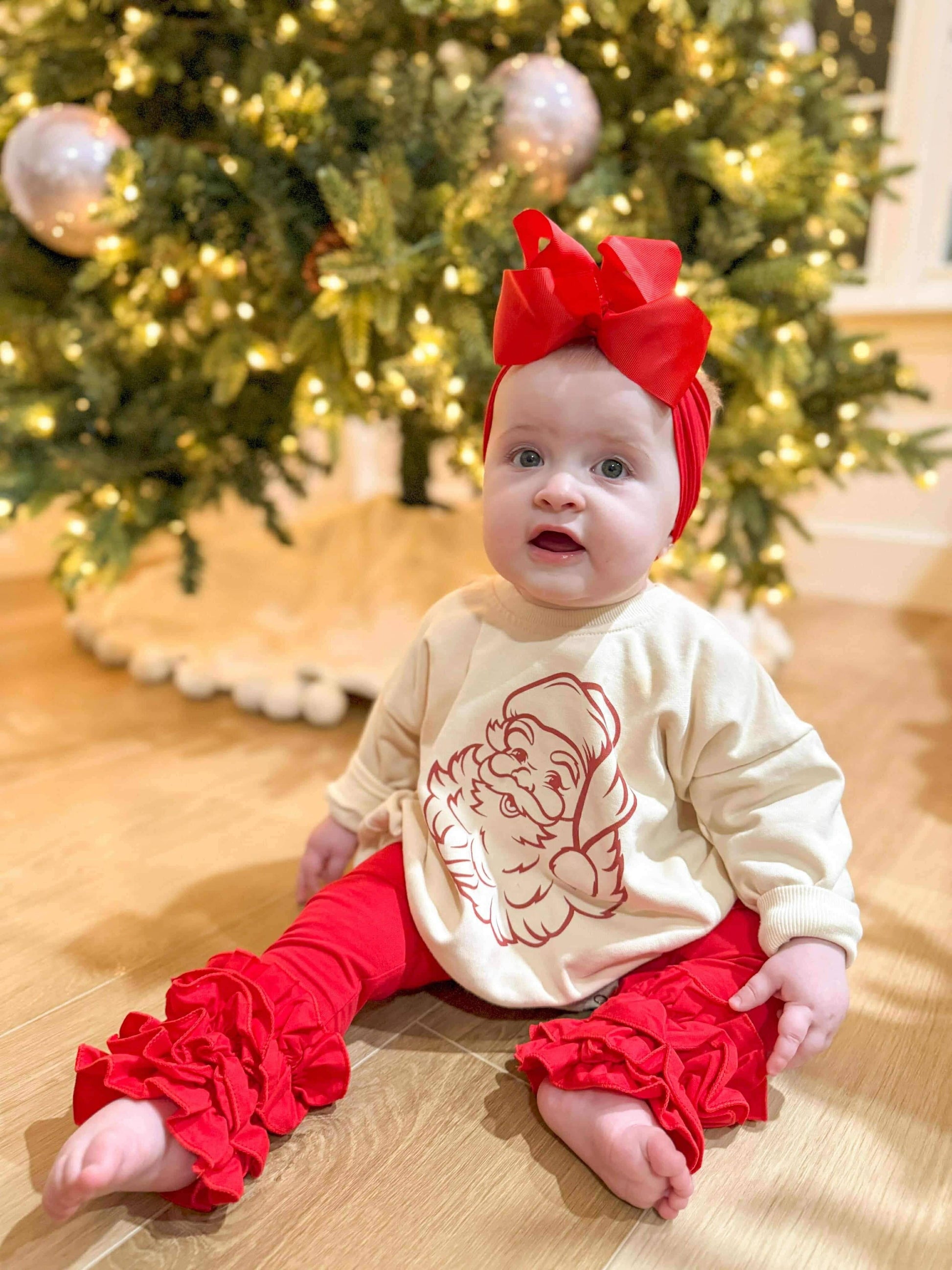 Baby in red and white outfit with Christmas tree in background