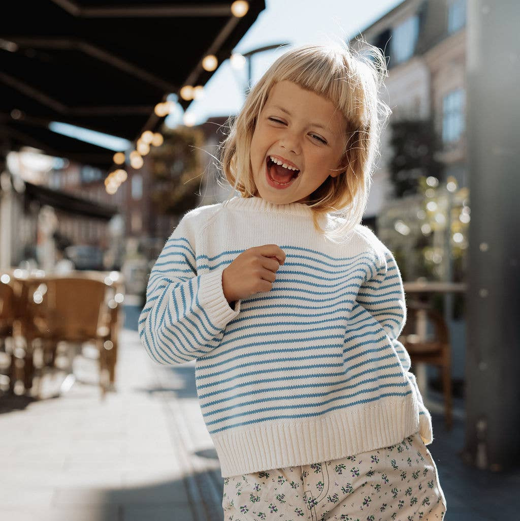 Child wearing a striped sweater and patterned pants outdoors