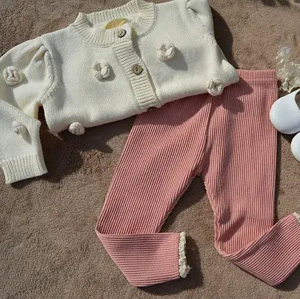 White knitted sweater with floral details and pink ribbed pants on a textured surface.