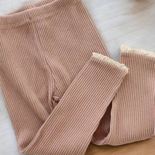 Folded ribbed pink leggings on a light wooden surface with a pine cone.