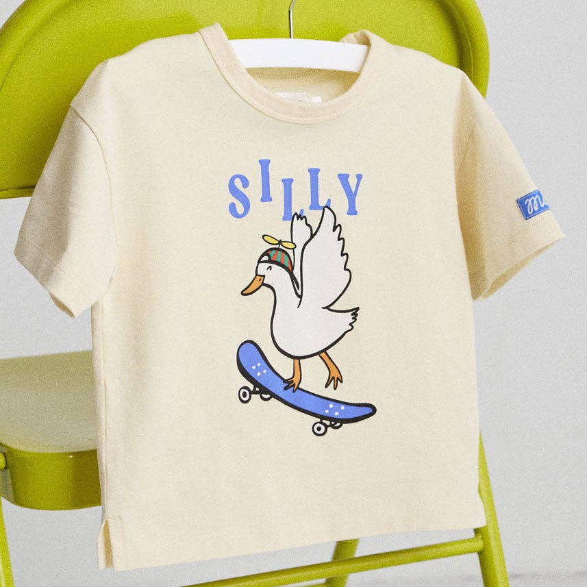 Beige t-shirt with a duck graphic and 'SILLY' text on a green chair.