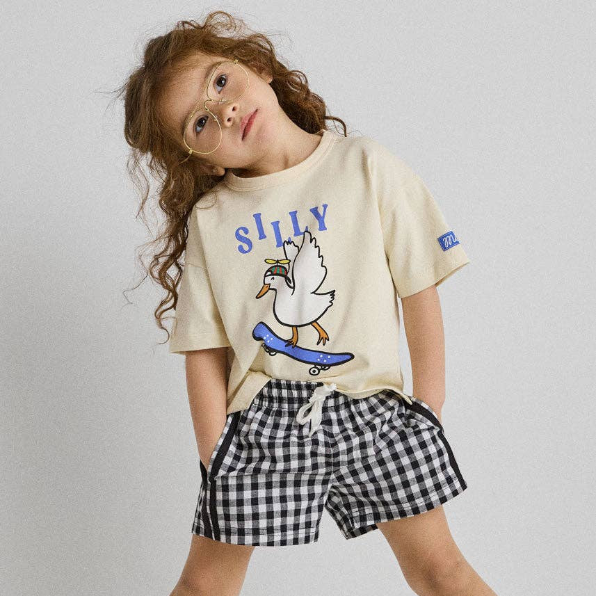 Child wearing a 'Silly' t-shirt with a duck graphic and checkered shorts on a plain background