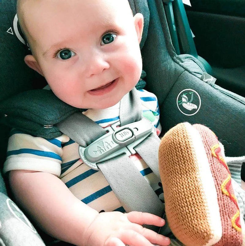 Baby in a car seat with a toy, looking at the camera.