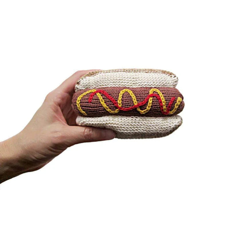 Hand holding a knitted hot dog toy with a white background