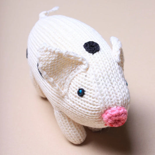 White knitted pig toy with black eyes and a pink nose on a beige background